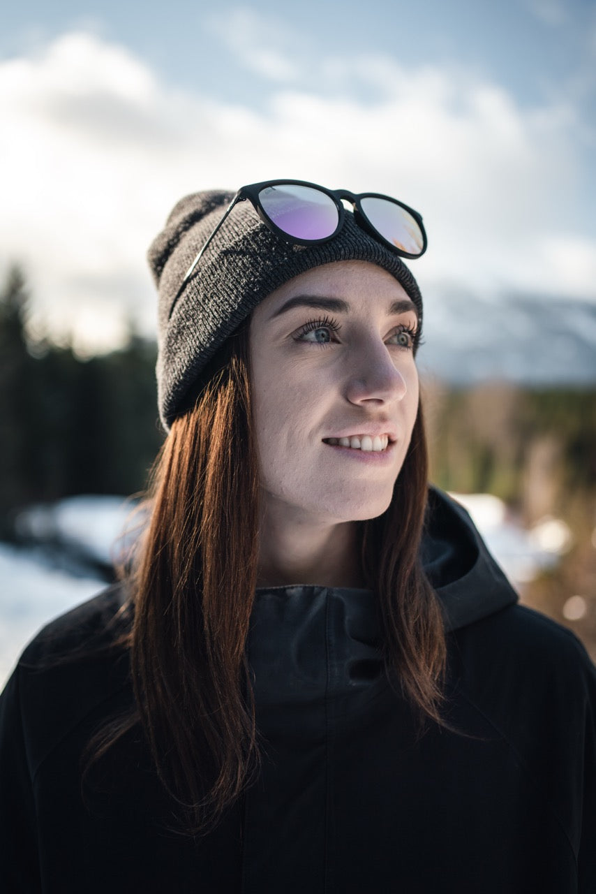 Man wearing mirrored goggles and gray beanie, holding skis in a snowy setting.