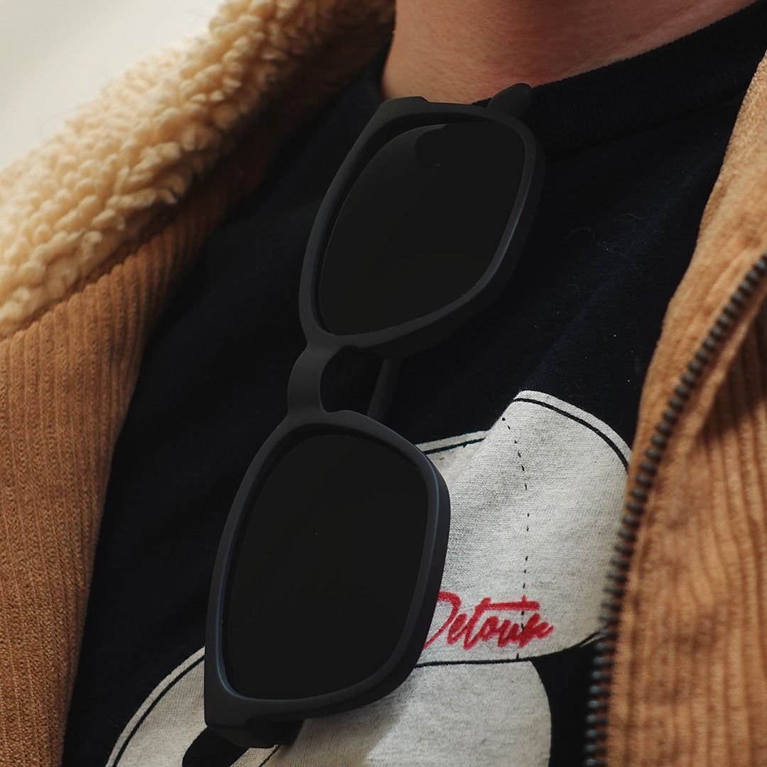 Man wearing mirrored goggles and gray beanie, holding skis in a snowy setting.